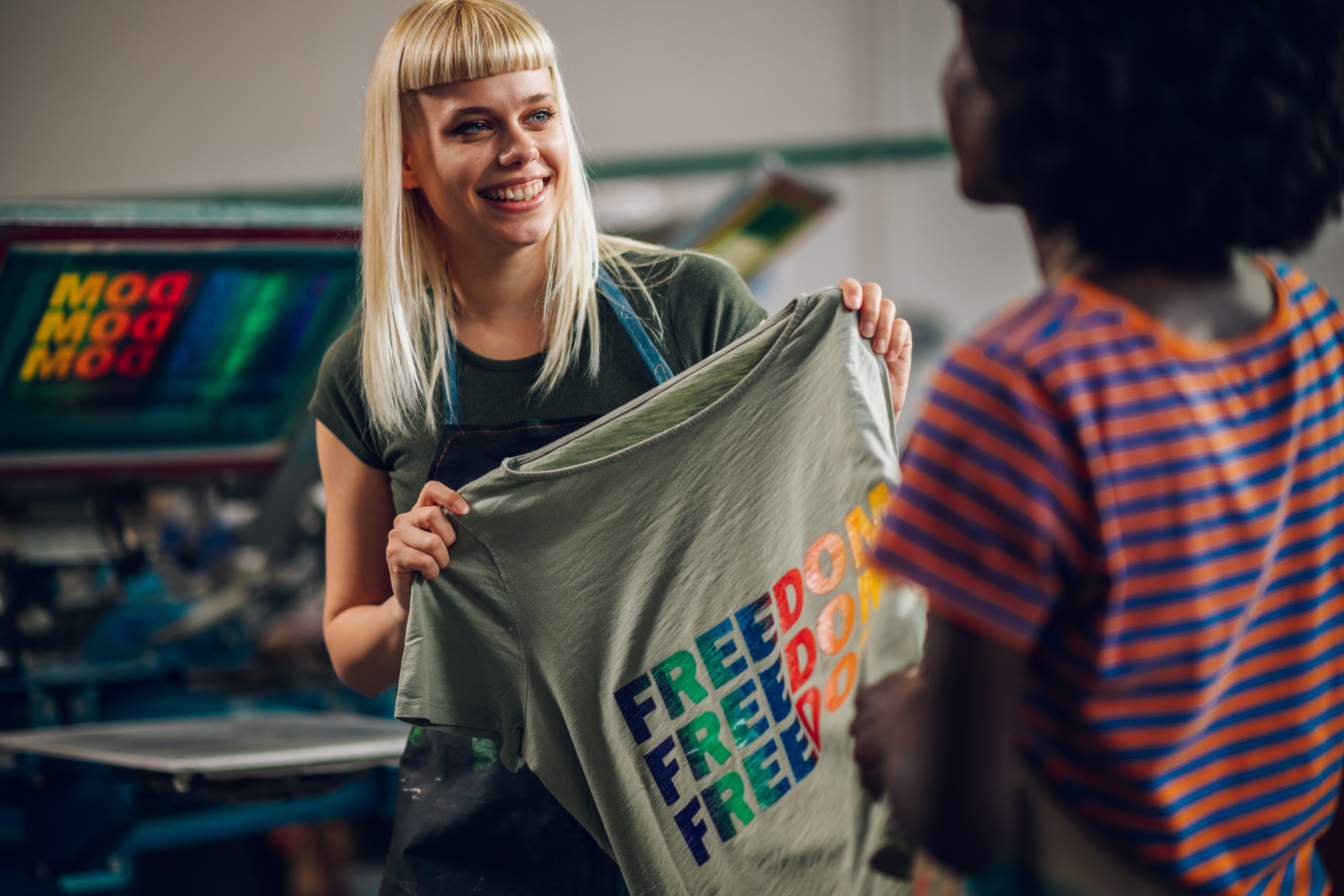 Smiling printing shop worker showing screen printed shirt to supervisor